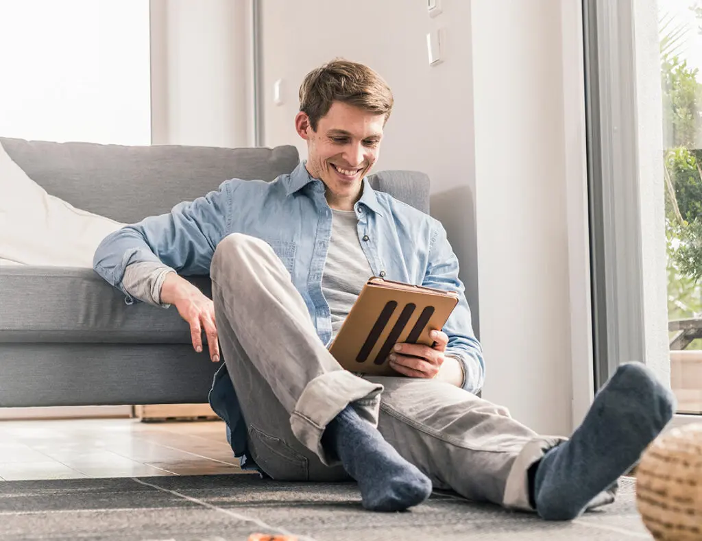 Homem tranquilo em casa lendo no tablet Necel corretora de seguros